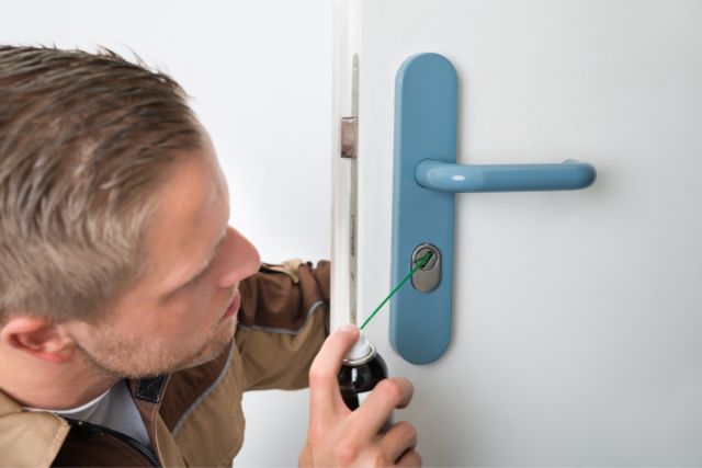 A locksmith lubricating a door lock using aeroseol.