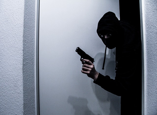 A burglar entering a home with a gun in hand.