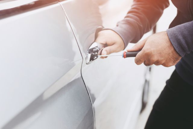 A man picking his car lock with a screw driver