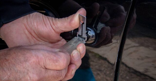 A pair of hands doing a door lock repair on a black car.