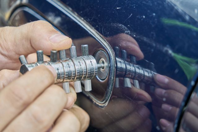 An automotive locksmith picking the lock of a blue car.