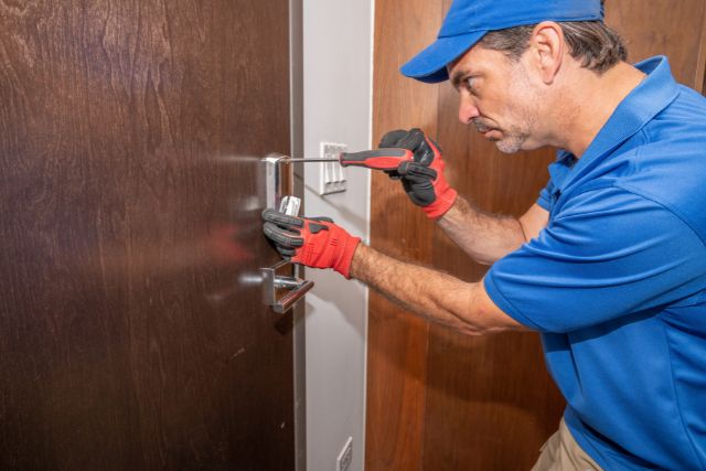 A professional locksmith opening a deadbolt with a screwdriver.