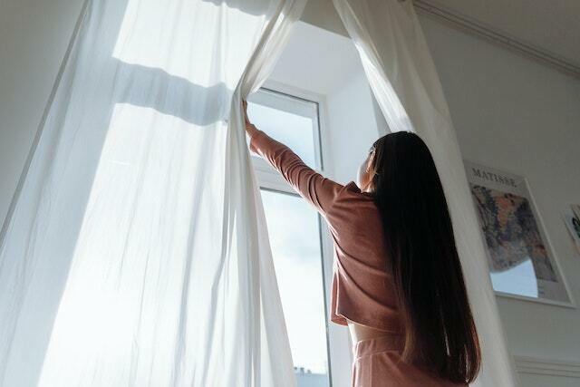 A woman opening a curtain to open the window.