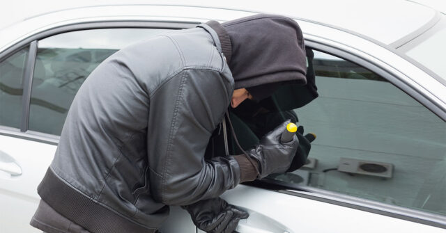 Man in black hoodie trying to break into a car with a screwdriver