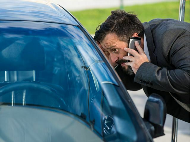 Man locked out of car, looking in the window while calling locksmith.
