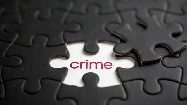 Black pieces of a puzzle with one missing. Under this piece is the word crime in red writing.