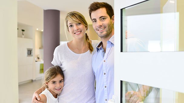 Couple with child standing in their secured home with door open.