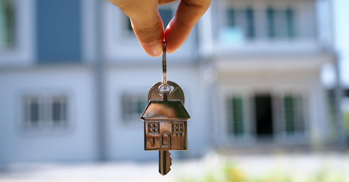 Person holding house keys in front of blurred house in the background