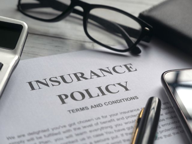 Insurance policy document with reading glasses, pen, phone and calculator