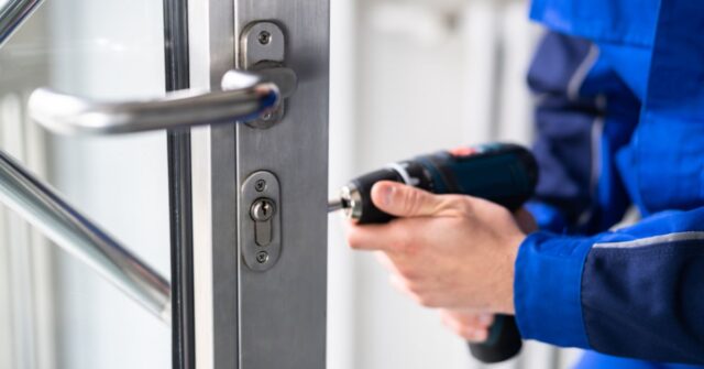 Locksmiths replacing a lock with an electric screwdriver.