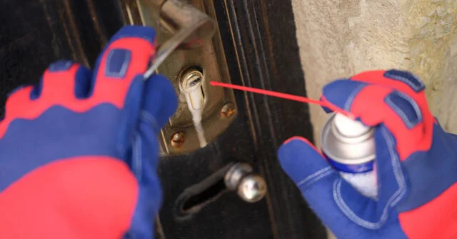 Person spraying a lubricant into a door lock with excess lubricant spilling out and running down the lock.