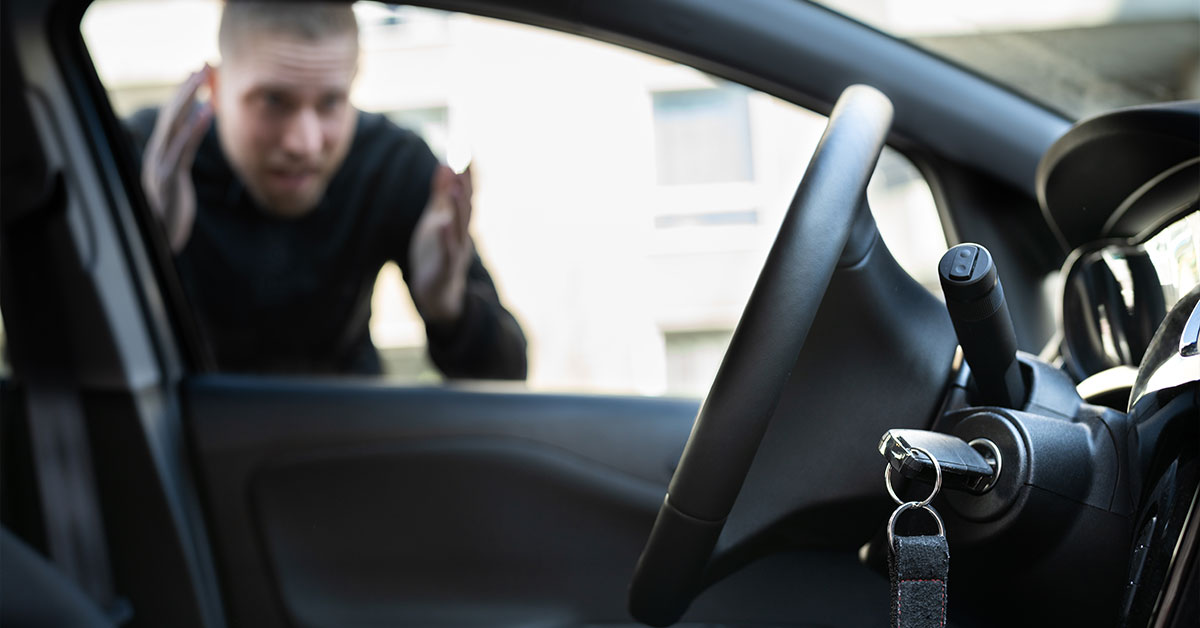 Man standing outside of car looking in through window to see the keys are in the ignition